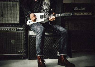 man wearing blue denim jeans playing white and black electric guitar sitting on black guitar amplifier